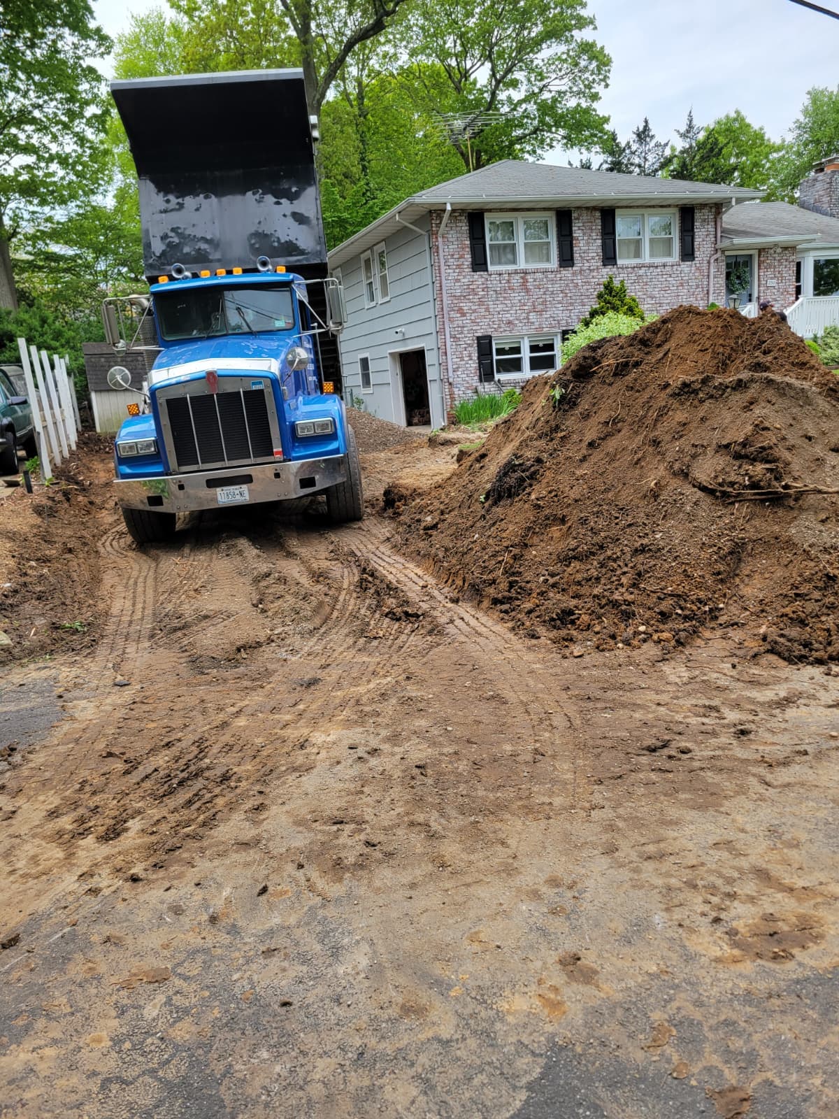 Blue dump truck with raised bed parked on a muddy driveway beside a dirt pile.
